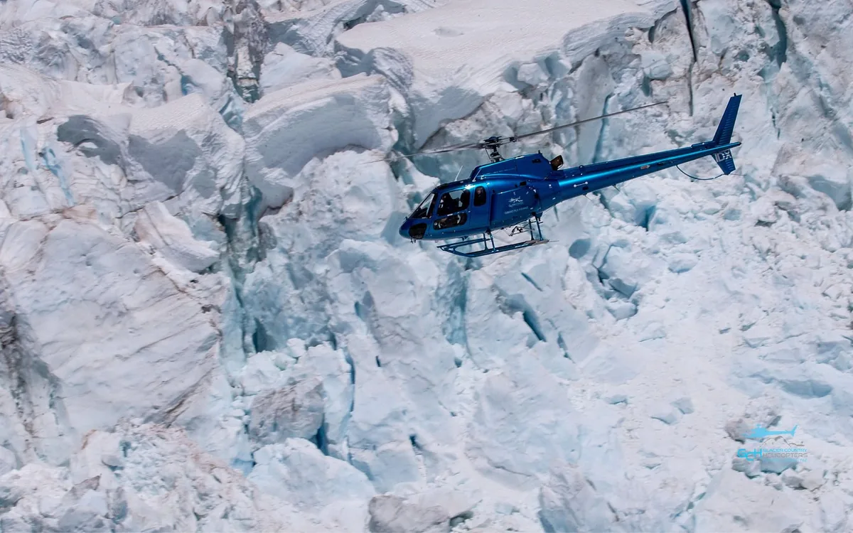 A helicopter flying past blue seracs on the glacier
