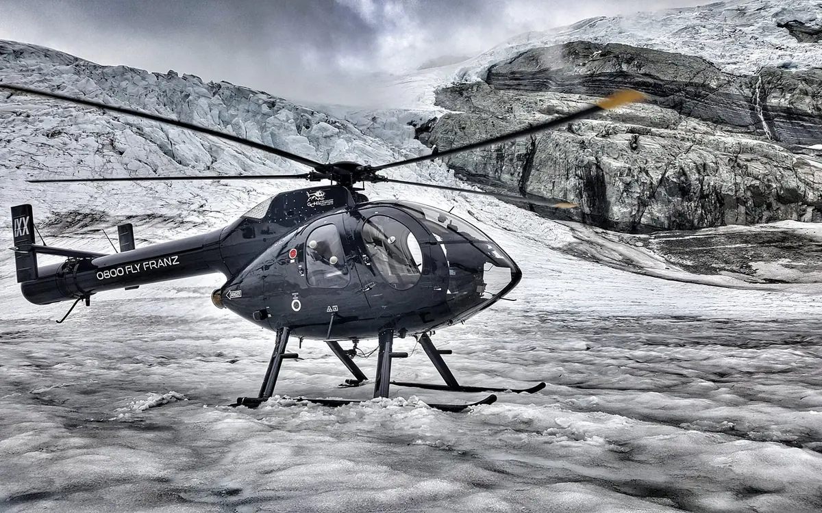 A helicopter shut down on the ice of Franz Josef Glacier with passengers beside it