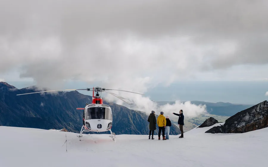 A helicopter landed on snow above Franz Josef Glacier with passengers beside it