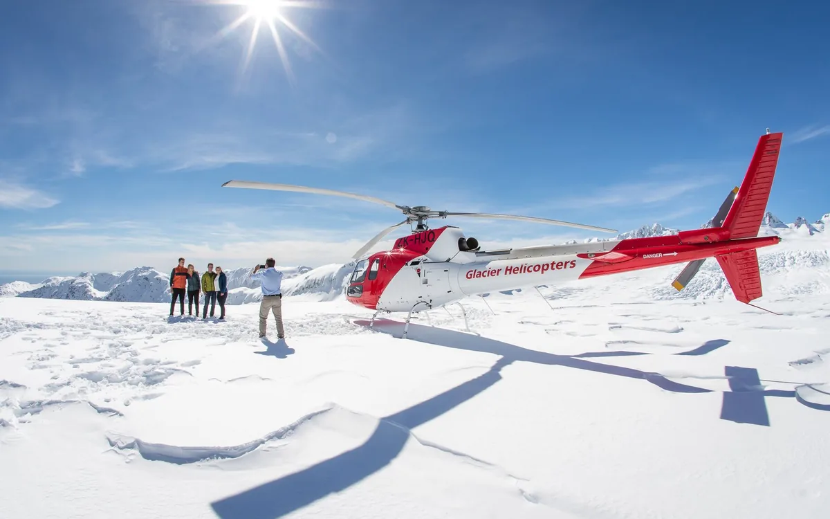 A helicopter landed on snow with passengers standing beside it